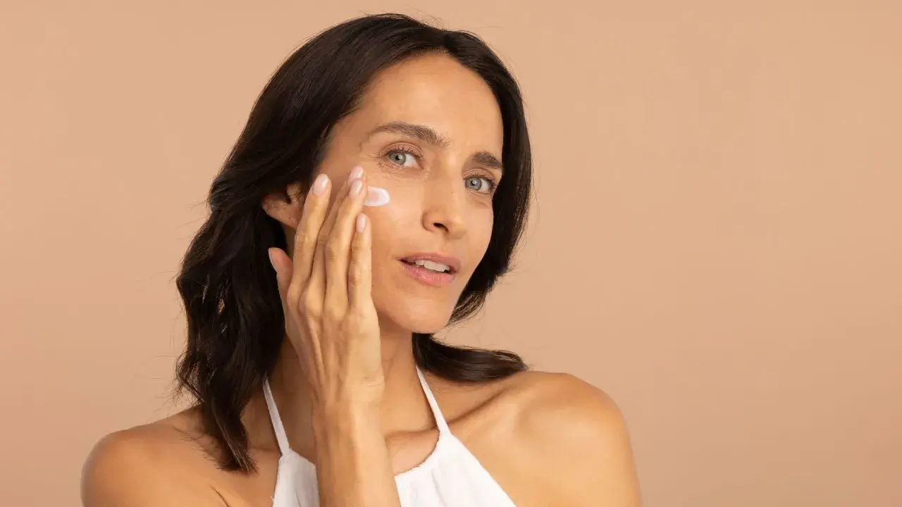 Une femme applique une crème sur son visage, profitant des bienfaits de l'hydratation pour une peau radieuse.