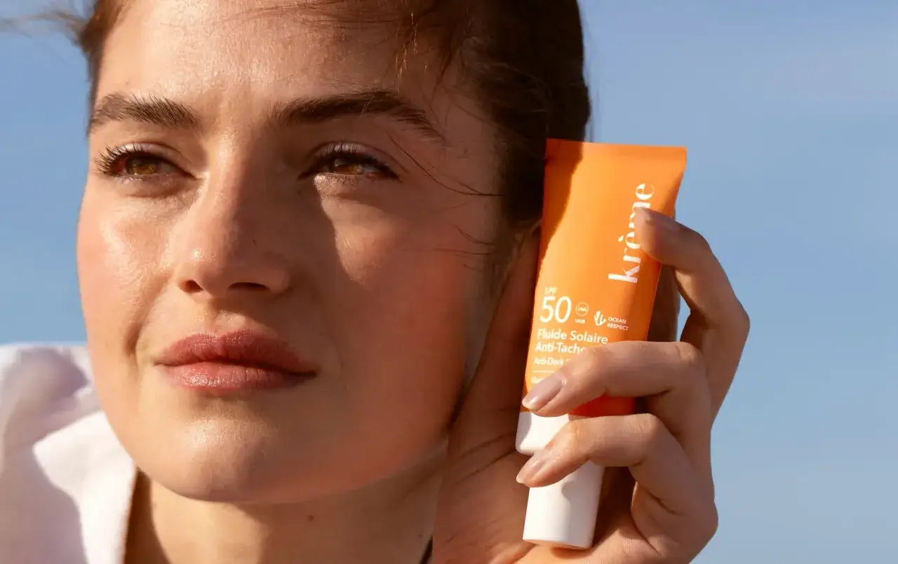 Une femme tient un tube de cr&egrave;me solaire SPF 50. L'effet cr&egrave;me solaire sur la peau est visible, prot&eacute;geant du soleil.
