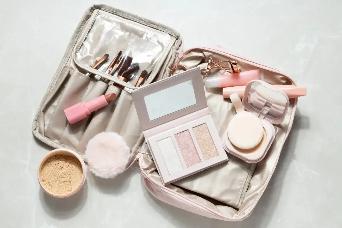 Une trousse de maquillage bagage cabine ouverte, révélant pinceaux, rouge à lèvres, palette d'highlighters, poudre et gloss.