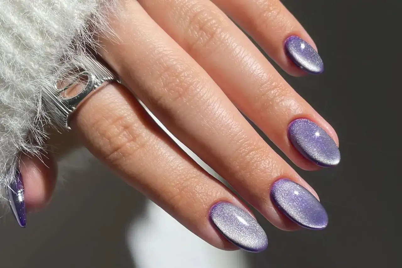 Main d'une femme avec une manucure cor&eacute;enne aux ongles violets brillants, style &oelig;il de chat.