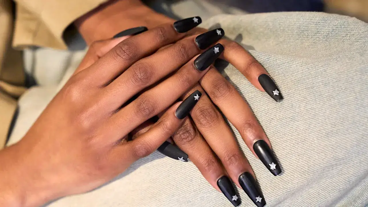 Mains aux ongles mat noirs, ornés d'étoiles scintillantes. Un look audacieux et chic.