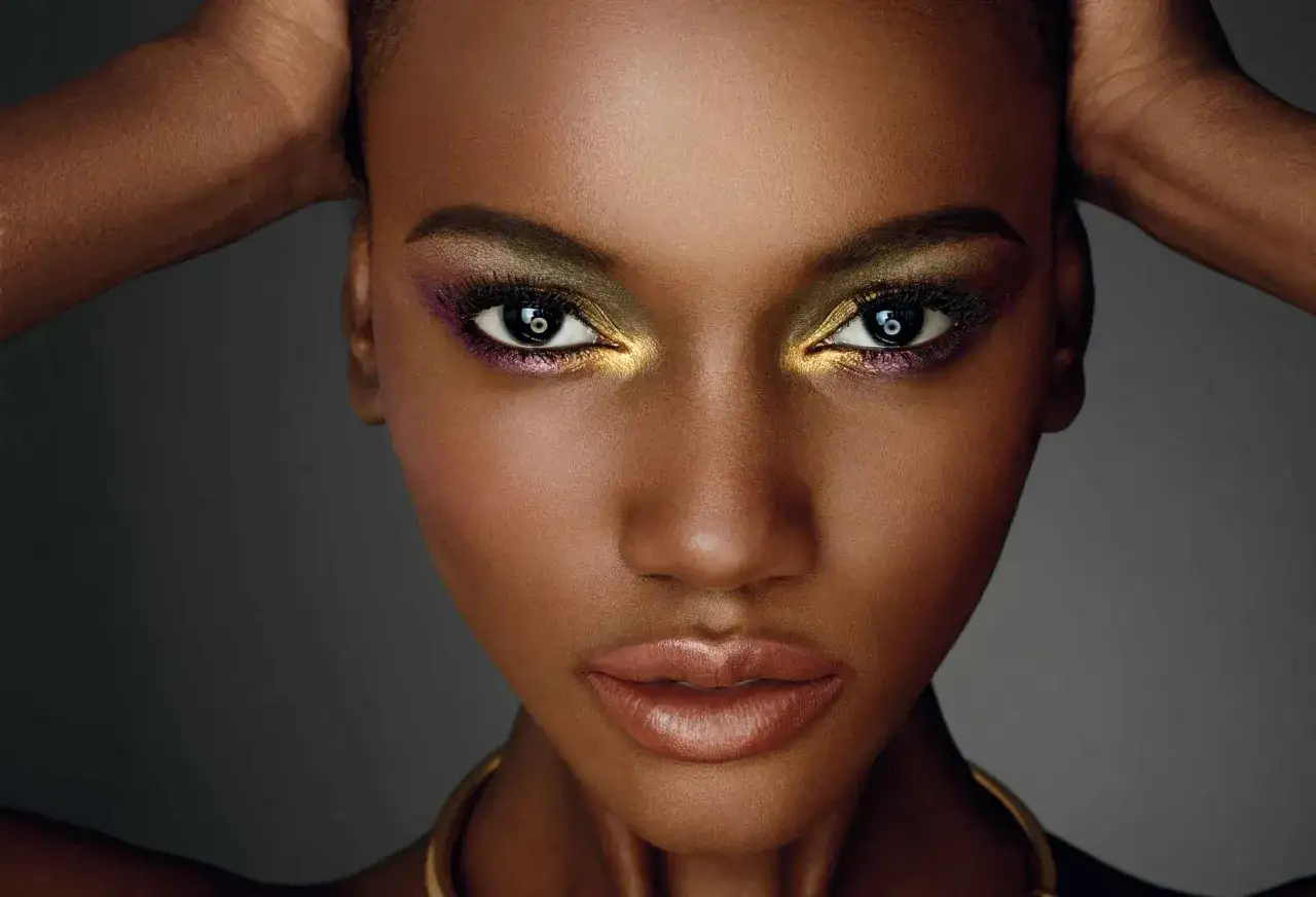 Un maquillage soir&eacute;e dor&eacute; et audacieux illumine le regard d'une femme, rehauss&eacute; de touches violettes. Ses l&egrave;vres sont subtilement gloss&eacute;es.
