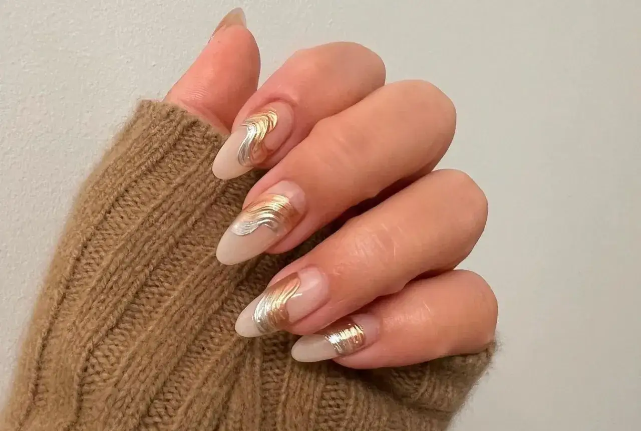 Manucure &eacute;l&eacute;gante avec un dessin ongles gel or et argent&eacute;, rappelant des vagues m&eacute;talliques sur une base nude.