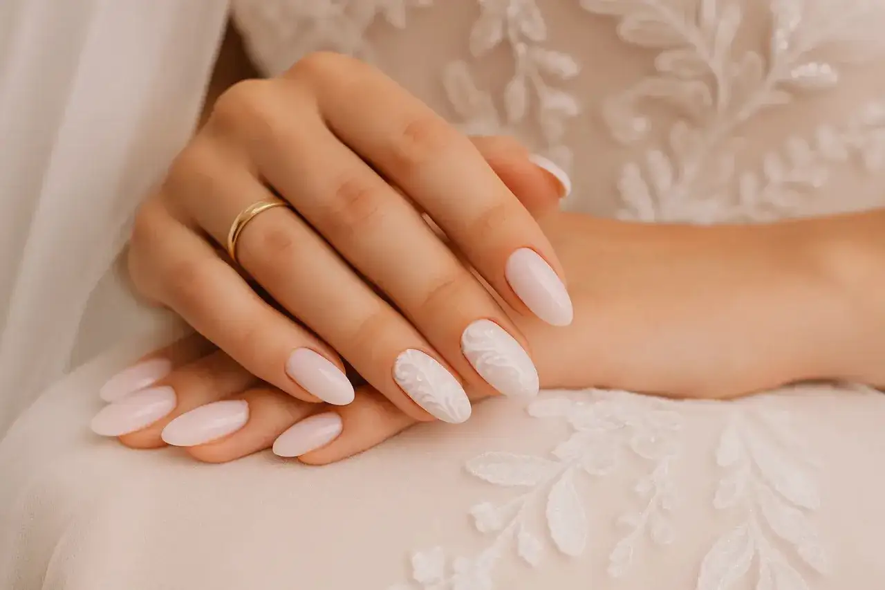 Mains d&eacute;licates orn&eacute;es d'ongles mariage d'un rose p&acirc;le subtil, dont un accent est mis sur un motif dentelle blanc. Une alliance dor&eacute;e brille sur l'annulaire.