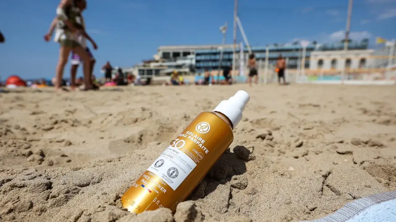 Flacon de cr&egrave;me solaire indice 50 sur le sable. Combien de temps avant de bronzer ? La plage est anim&eacute;e en arri&egrave;re-plan.