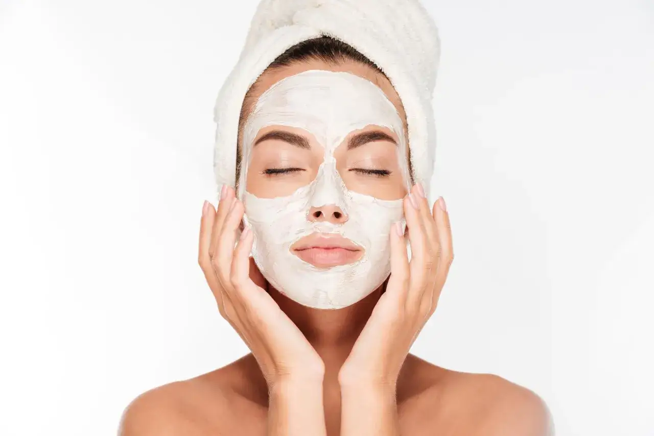 Une femme avec une serviette sur la tête applique un masque blanc sur son visage, espérant réduire les cicatrices d'acné.