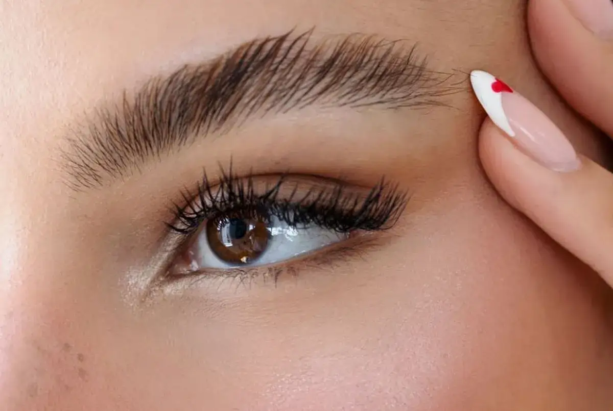 Un œil marron aux cils longs et fournis, sublimé par un maquillage discret. Un ongle manucuré avec un cœur rouge attire le regard.