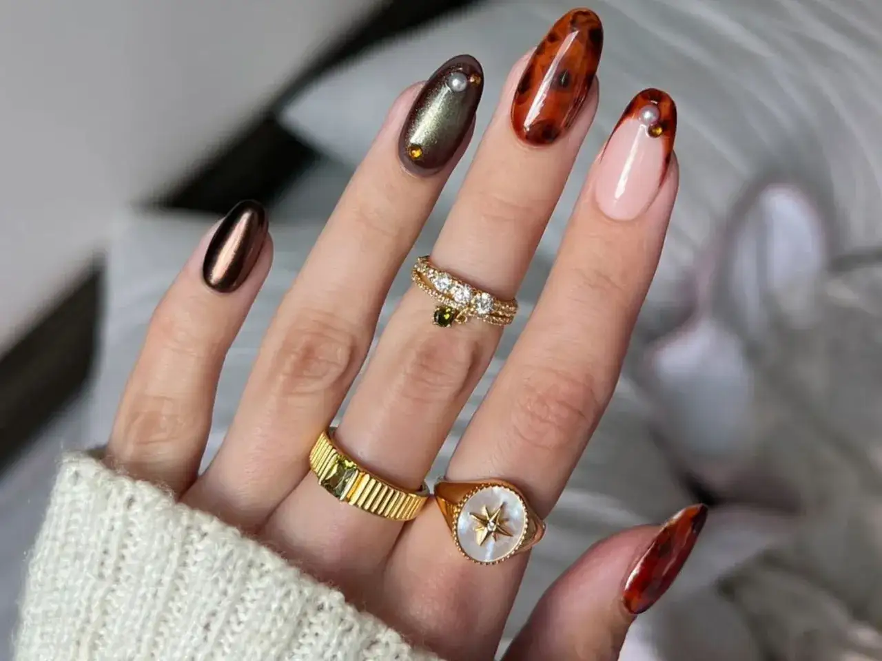 Main d'une femme portant des bijoux et des ongles ornés d'un motif écaille de tortue.