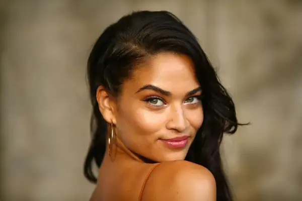 Un regard intense sous ton olive, une peau dorée, des boucles sombres et des créoles dorées.